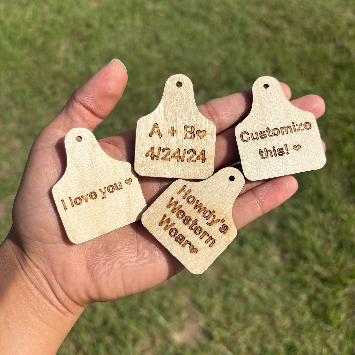 Hand holding four wooden tags with engraved text against a grassy background