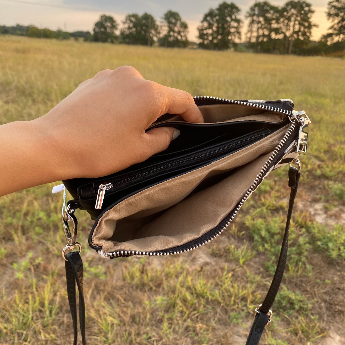 Hand holding an open handbag against a natural background with trees and grass.