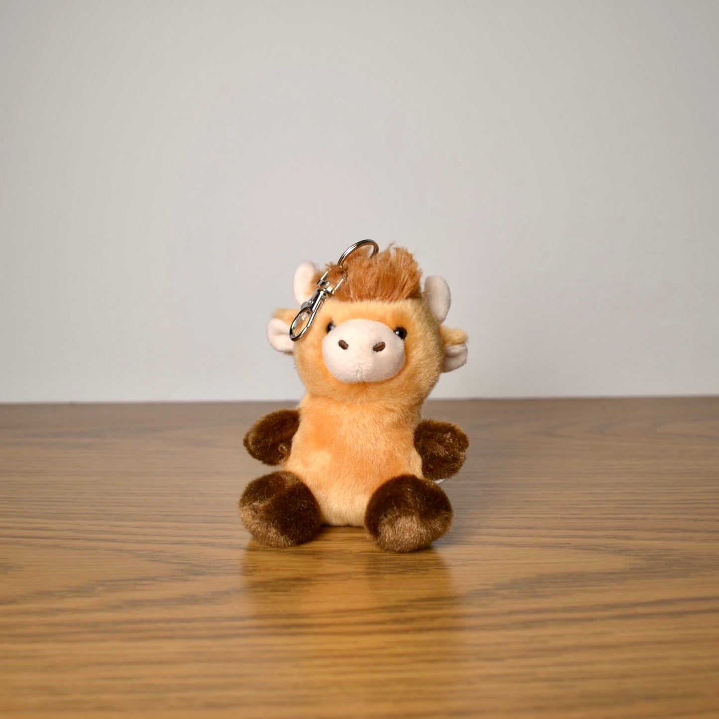 Plush cow keychain on a wooden surface with a plain background