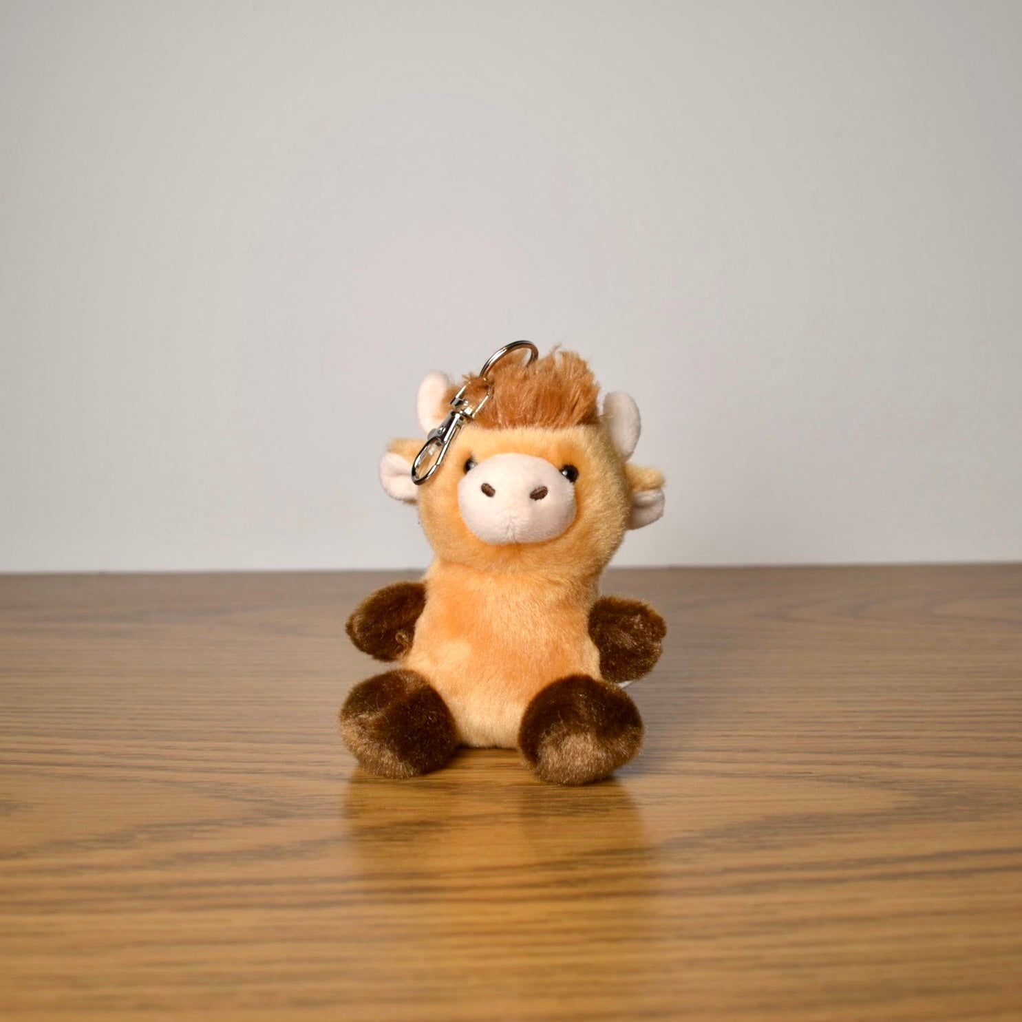 Plush cow keychain on a wooden surface with a plain background