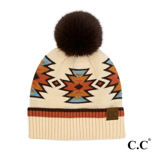 A beanie with a geometric pattern featuring multiple colors and a brown pom-pom on top on a white background