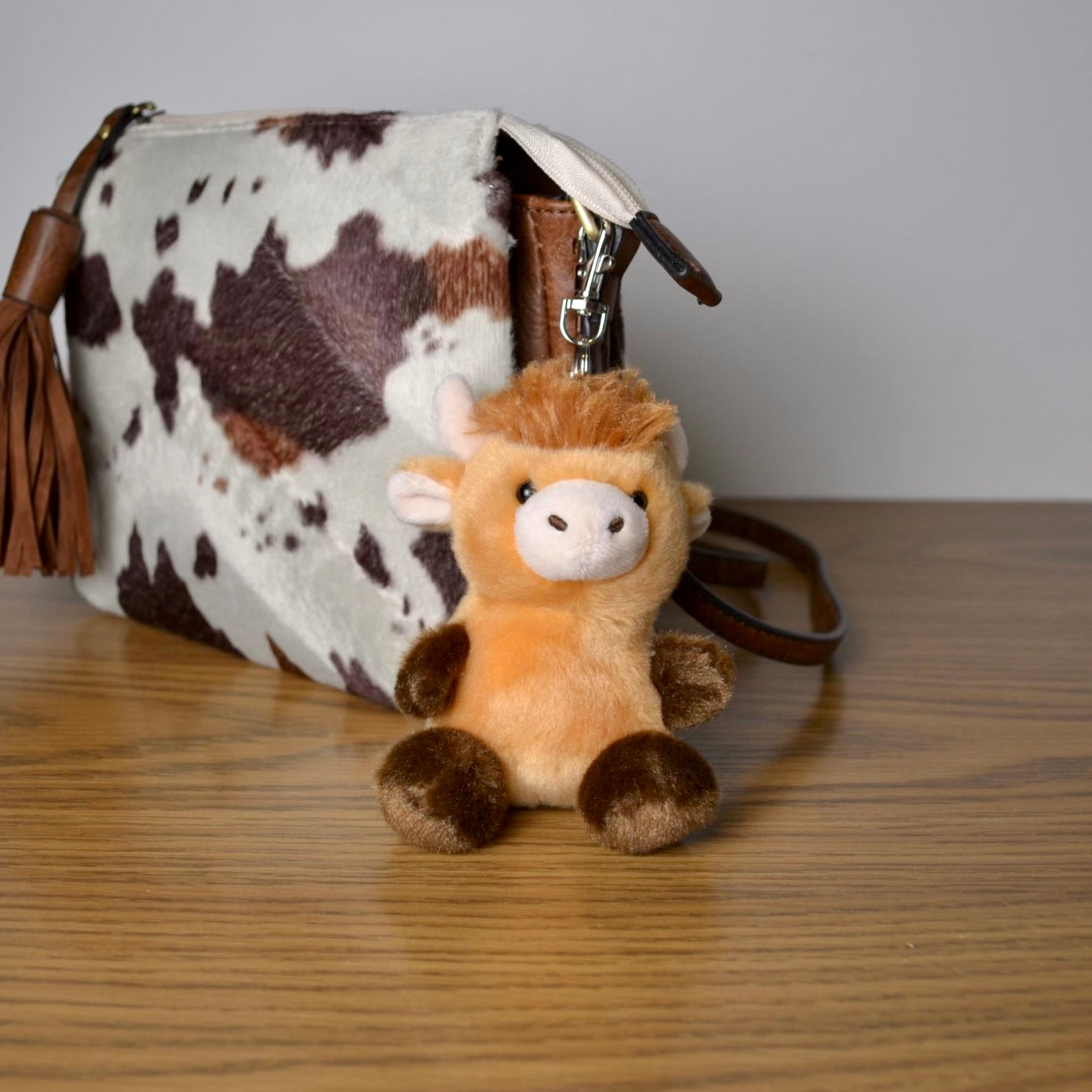 Plush cow keychain attached to a cow print bag on a wooden surface