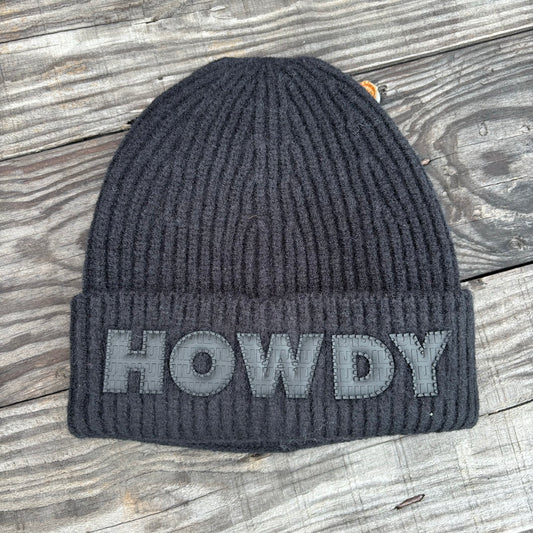black beanie that says 'howdy' on a wooden table